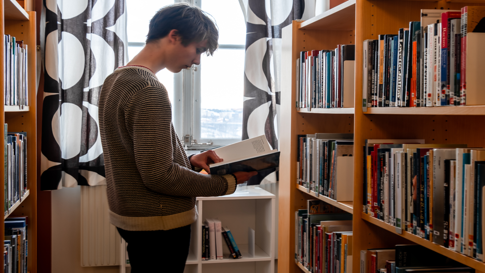 Elev bläddrar i bok i bibliotek, foto. 